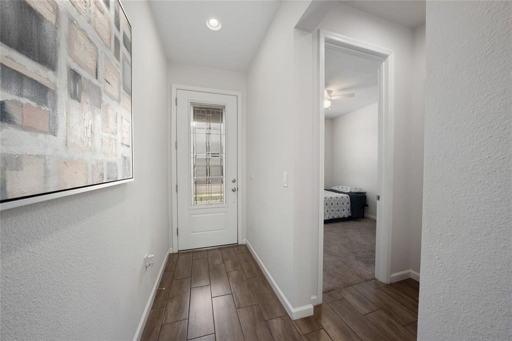 A bright entryway with wood-look tile flooring leads to a front door and a bedroom — 5610 WESTERN SUN DRIVE, ST CLOUD, FL