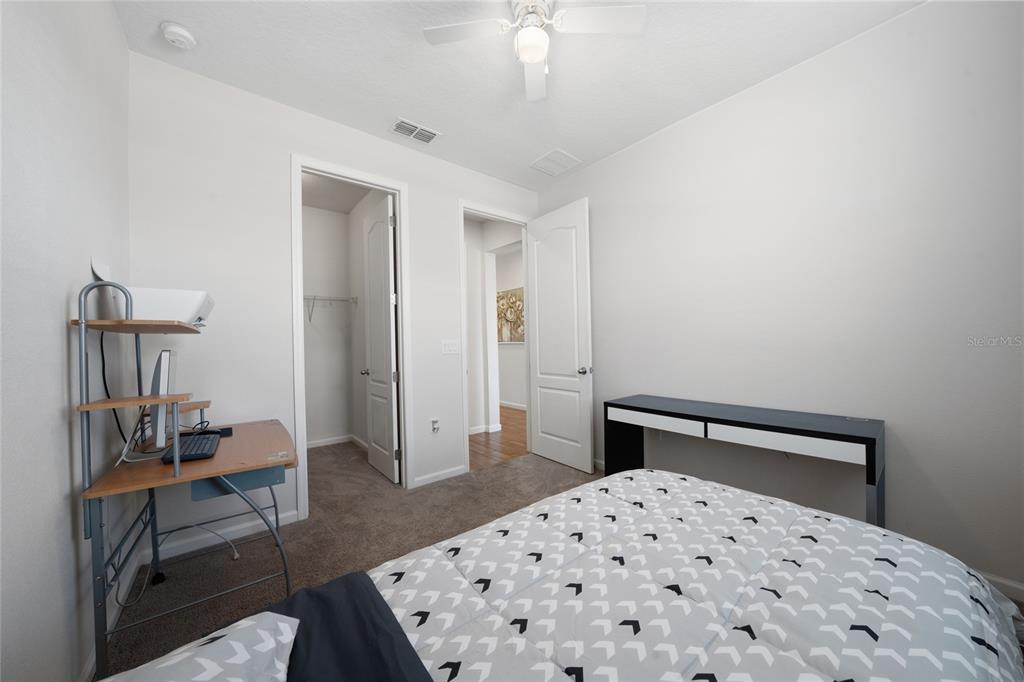 A bedroom with a desk, a bed with a patterned comforter, and two open doorways — 5610 WESTERN SUN DRIVE, ST CLOUD, FL