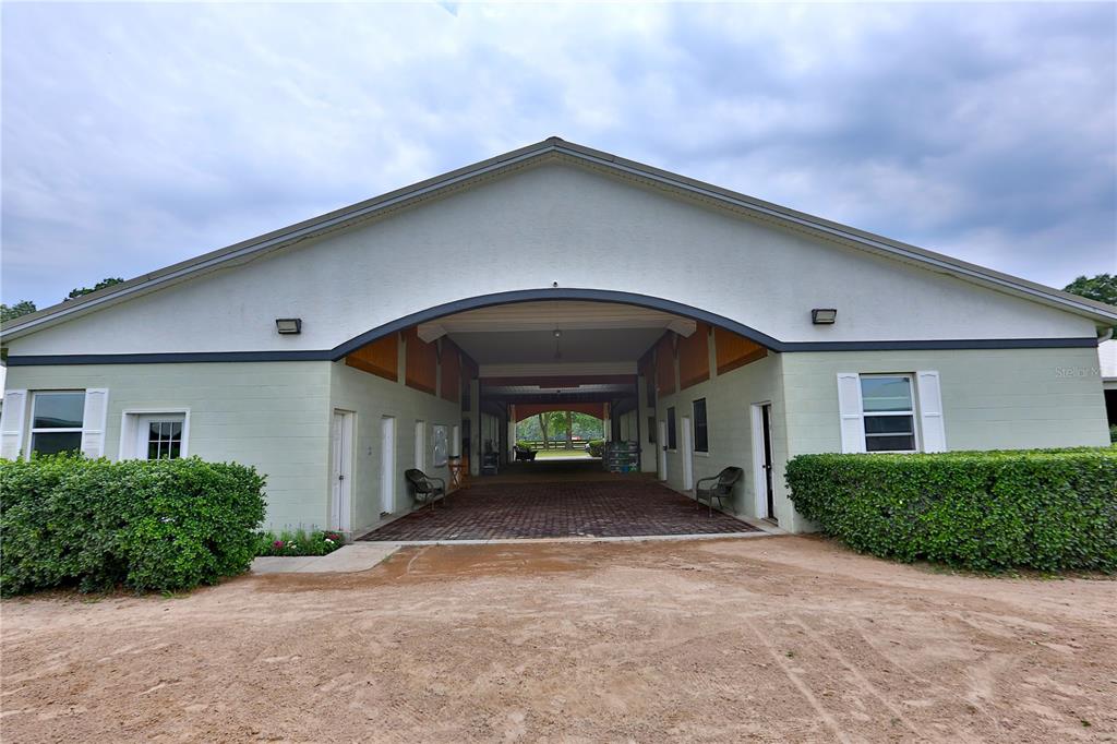 A wide, covered breezeway connects two sides of a light-colored, single-story horse barn — 19431 NE 17TH PLACE, WILLISTON, FL