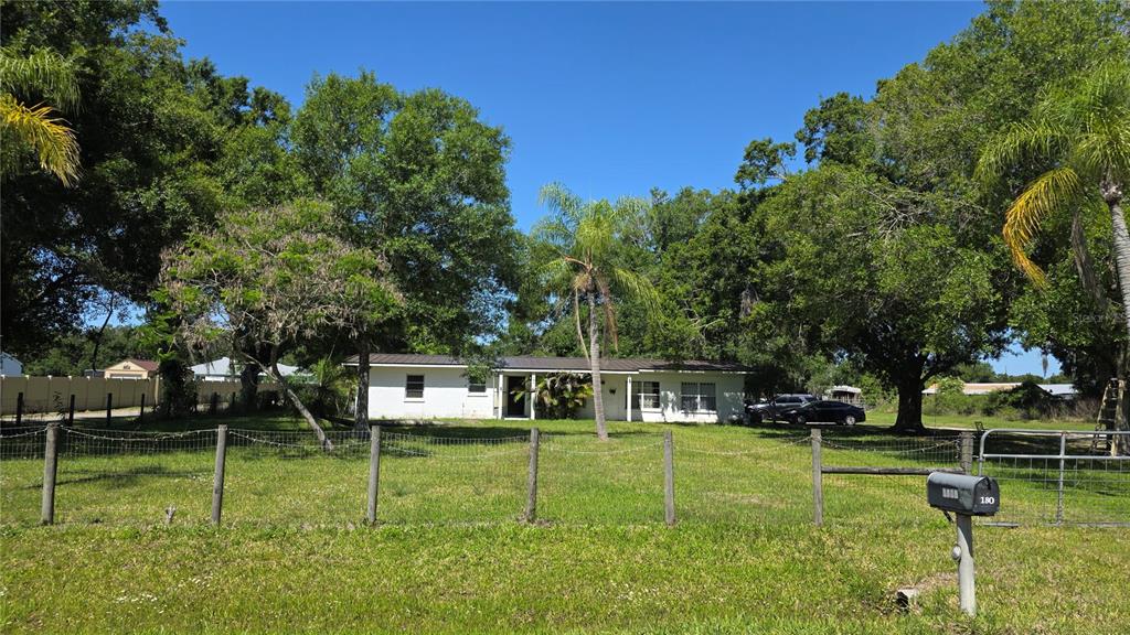A single-story white house sits behind a wire fence on a grassy lot — 1808 ZIPPERER ROAD, BRADENTON, FL