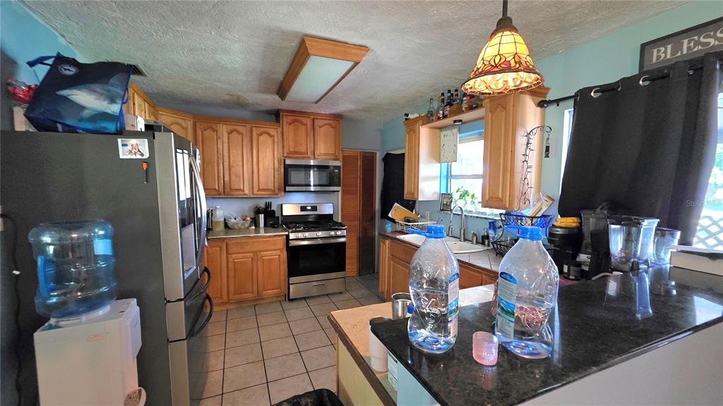 A kitchen features wood cabinets, stainless steel appliances, tile flooring, and a dark countertop — 1808 ZIPPERER ROAD, BRADENTON, FL