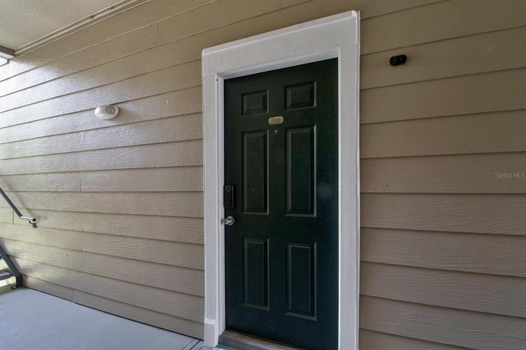 A dark green front door with a number plate is set in tan horizontal siding — 13103 MULBERRY PARK DRIVE UNIT 8211, ORLANDO, FL