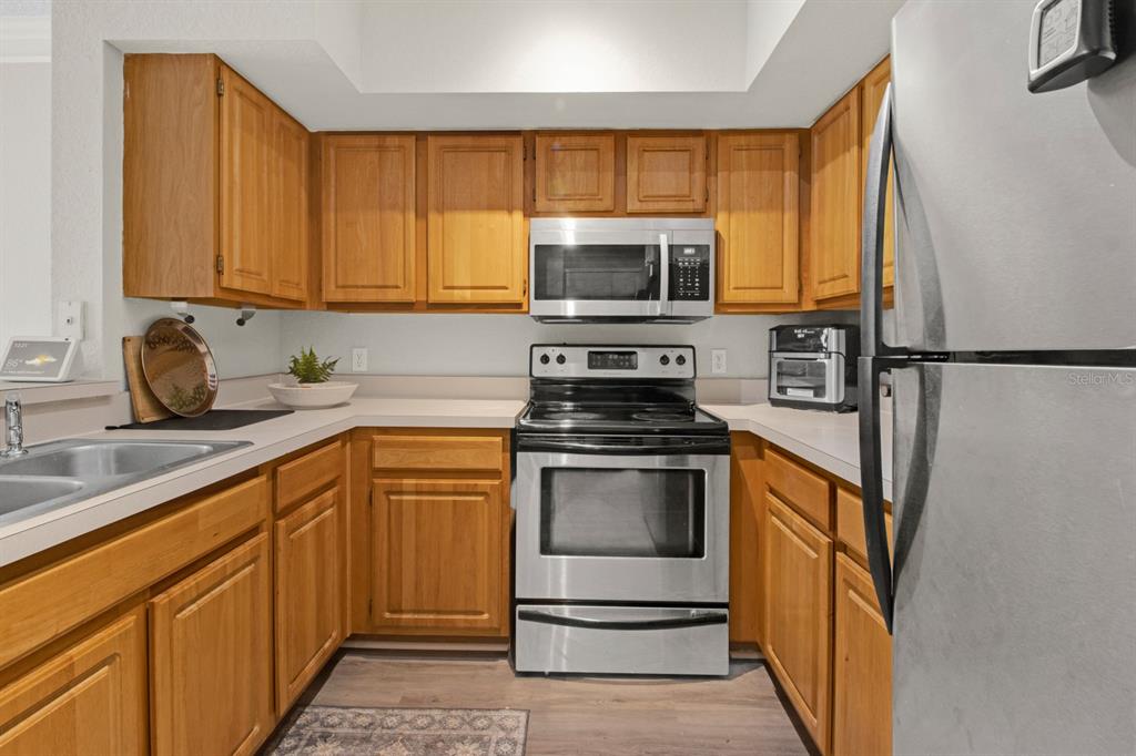A kitchen features wood cabinets, stainless steel appliances, and light-colored countertops — 13103 MULBERRY PARK DRIVE UNIT 8211, ORLANDO, FL