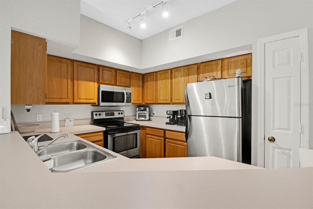 A kitchen features wood cabinets, stainless steel appliances, and a double sink on a peninsula — 13103 MULBERRY PARK DRIVE UNIT 8211, ORLANDO, FL