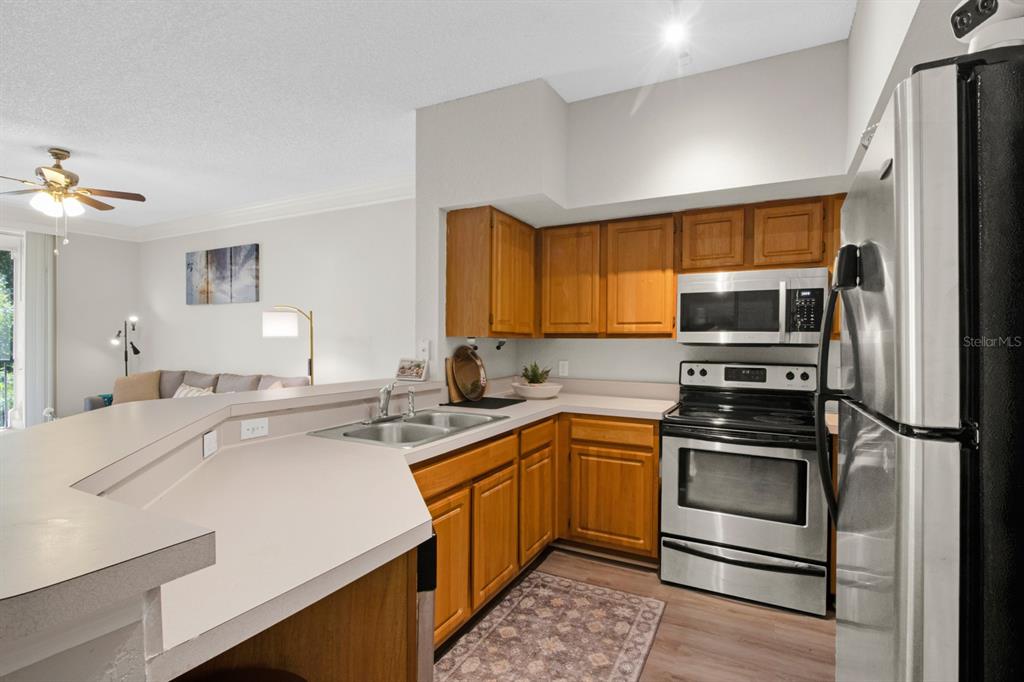 A kitchen with wood cabinets, stainless steel appliances, and a breakfast bar overlooking a living room — 13103 MULBERRY PARK DRIVE UNIT 8211, ORLANDO, FL