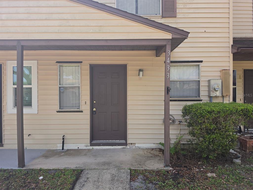 A beige two-story townhouse exterior features a brown front door and a concrete walkway — 3433 JOE MURELL DRIVE, TITUSVILLE, FL