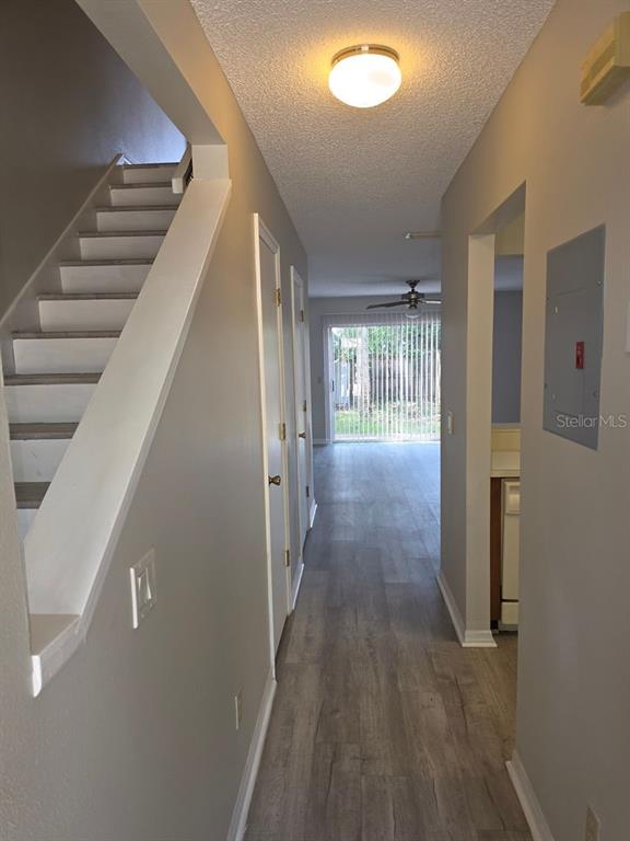 A hallway with light wood-look flooring leads past a staircase to a sliding glass door — 3433 JOE MURELL DRIVE, TITUSVILLE, FL