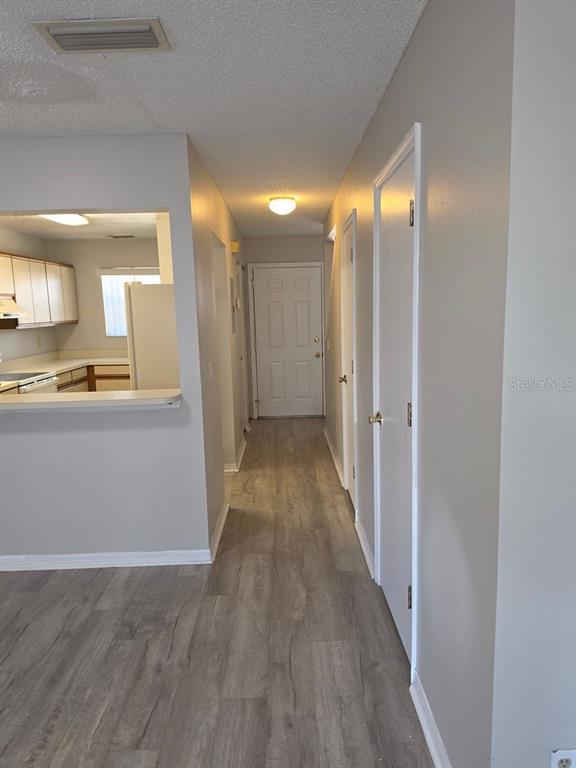 A hallway with light-colored walls and wood-look flooring leads to an exterior door — 3433 JOE MURELL DRIVE, TITUSVILLE, FL