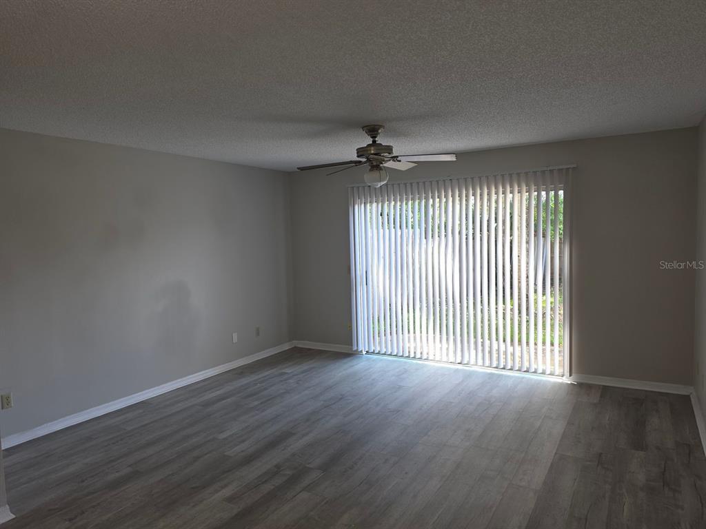 An empty living room features gray wood-look flooring, a ceiling fan, and vertical sliding glass doors — 3433 JOE MURELL DRIVE, TITUSVILLE, FL