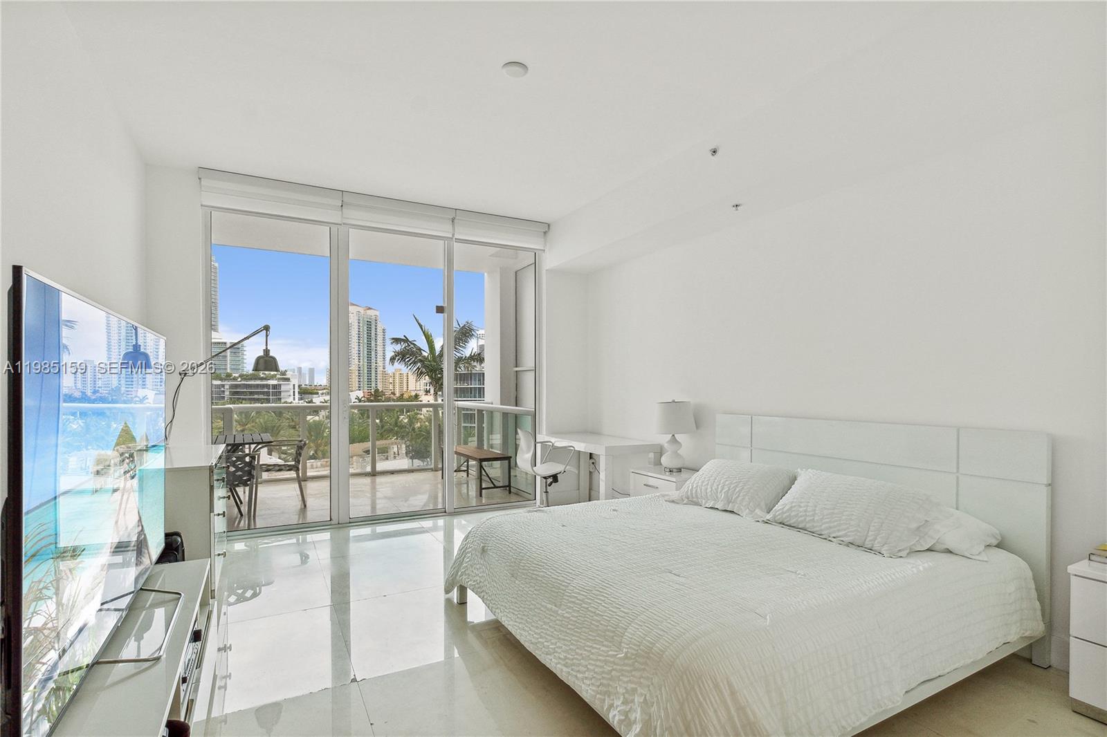 A modern bedroom features a white bed, a desk, and a balcony with city views — 50 S Pointe Dr # 805, Miami Beach FL 33139, MIAMI BEACH, FL