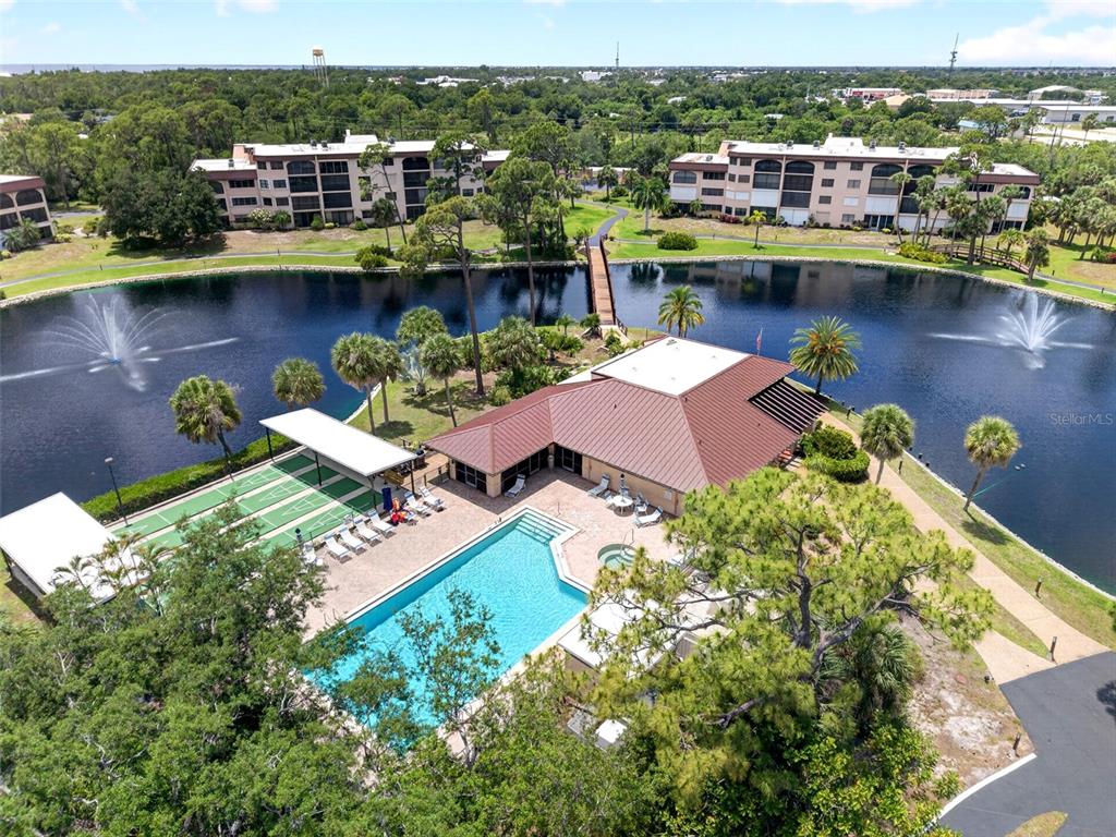 An aerial view shows a community pool, clubhouse, and shuffleboard courts surrounded by a lake — 23465 HARBORVIEW ROAD UNIT 214, PUNTA GORDA, FL