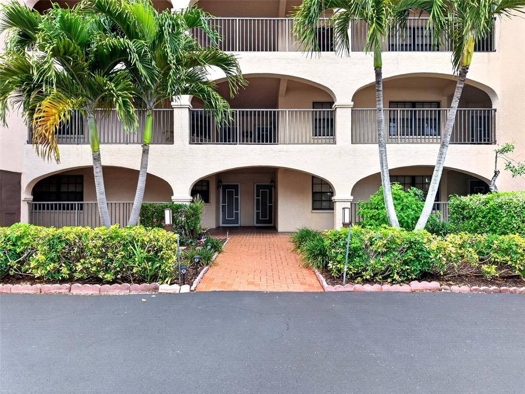 A multi-story building exterior features arched balconies, a brick walkway, and surrounding palm trees — 23465 HARBORVIEW ROAD UNIT 214, PUNTA GORDA, FL