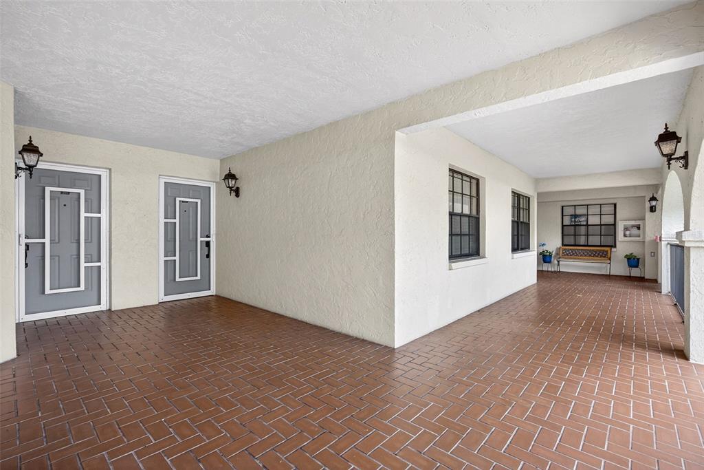 A covered outdoor walkway features a herringbone-patterned brick floor and two gray entry doors — 23465 HARBORVIEW ROAD UNIT 214, PUNTA GORDA, FL