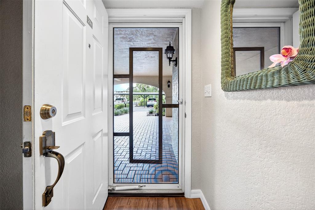 An open white front door reveals a screen door looking out onto a paved parking area — 23465 HARBORVIEW ROAD UNIT 214, PUNTA GORDA, FL
