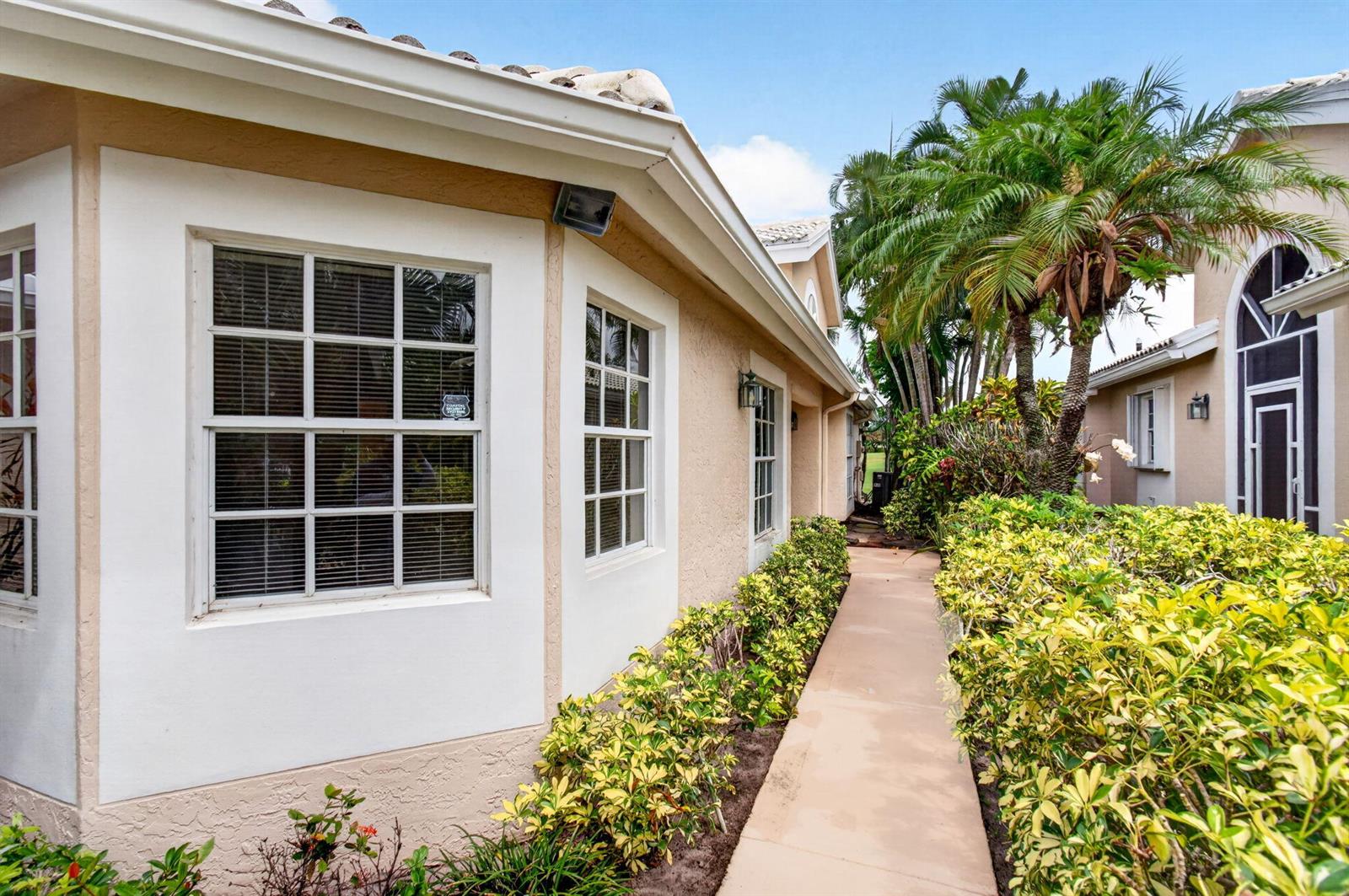 A beige house exterior features a concrete walkway lined with bushes and palm trees — 6071 Greenspointe Drive, Boynton Beach FL 33437, BOYNTON BEACH, FL