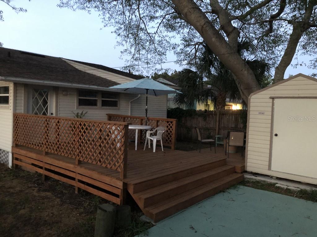 A wooden deck with a patio table and umbrella sits beside a house and shed — 6100 FLORIDA AVENUE, NEW PORT RICHEY, FL