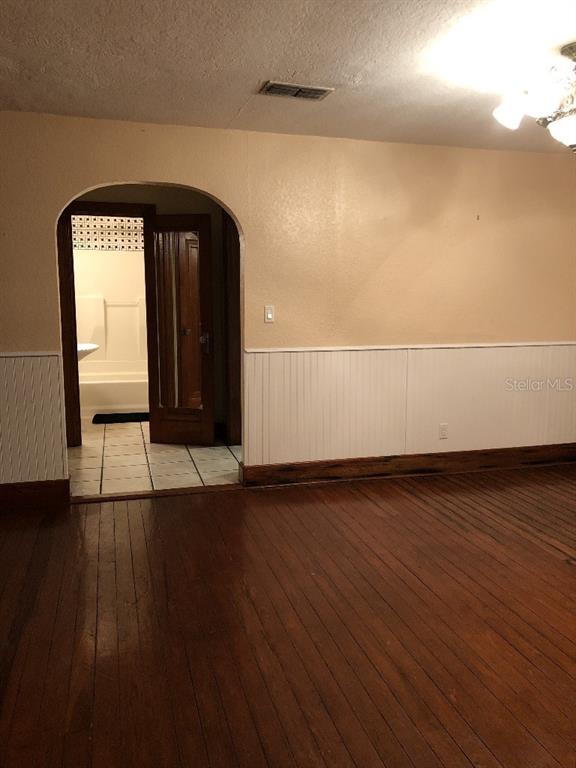 A room with hardwood floors and white wainscoting leads through an arched doorway to a bathroom — 6100 FLORIDA AVENUE, NEW PORT RICHEY, FL
