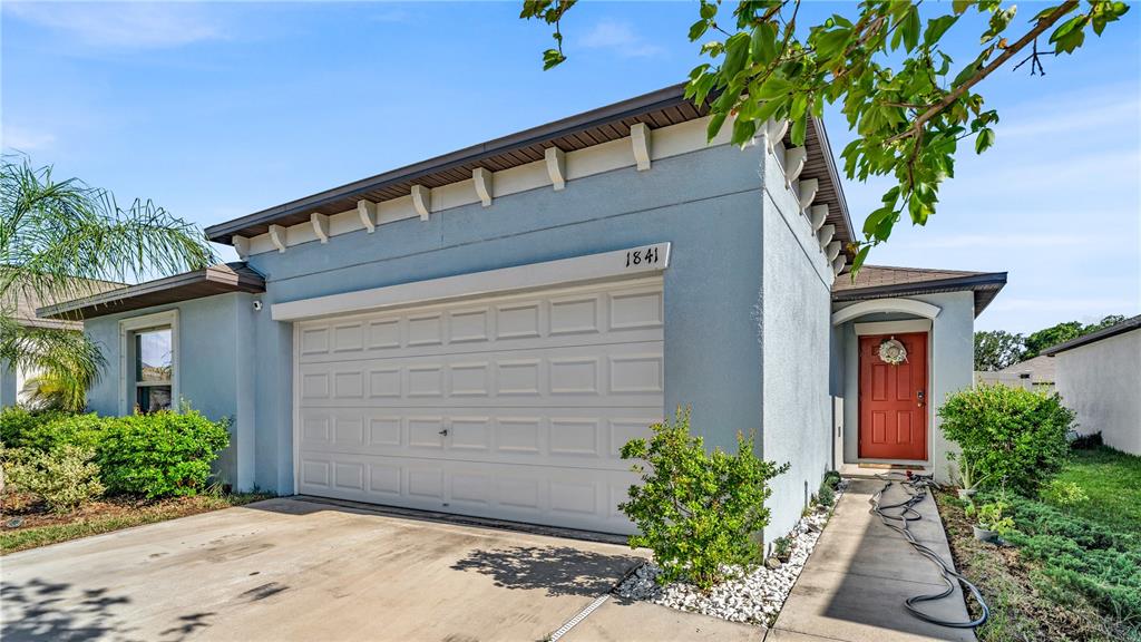 A single-story house with a light blue stucco exterior, a white garage door, and red door — 1841 CRINKLE LEAF COURT, RUSKIN, FL
