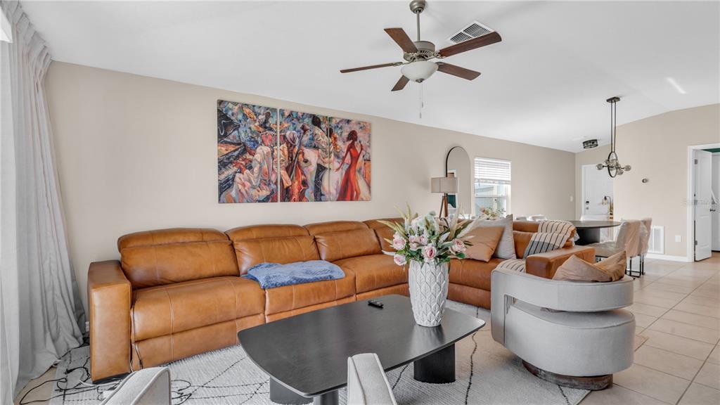 A living room features a tan leather sectional, a black coffee table, and abstract wall art — 1841 CRINKLE LEAF COURT, RUSKIN, FL