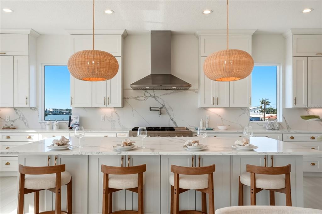A kitchen features a marble island with four wooden stools, white cabinetry, and two pendant lights — 534 CRYSTAL DRIVE, MADEIRA BEACH, FL