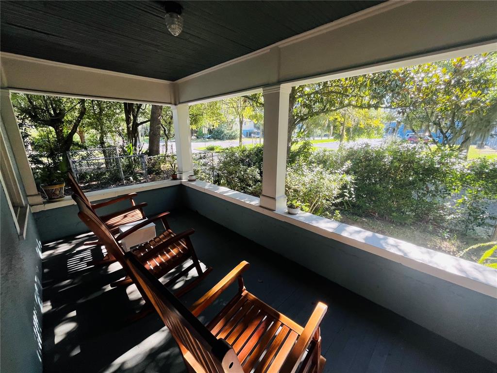 A covered porch features dark painted flooring, wooden rocking chairs, and views of surrounding trees — 1124 NW 4TH STREET NW, GAINESVILLE, FL