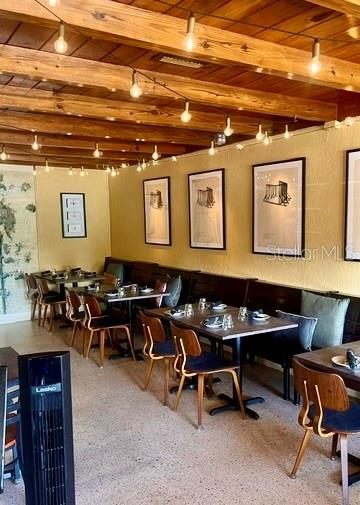 A restaurant dining room features wooden ceiling beams, string lights, and framed wall art — 1518 S DIXIE FREEWAY, NEW SMYRNA BEACH, FL