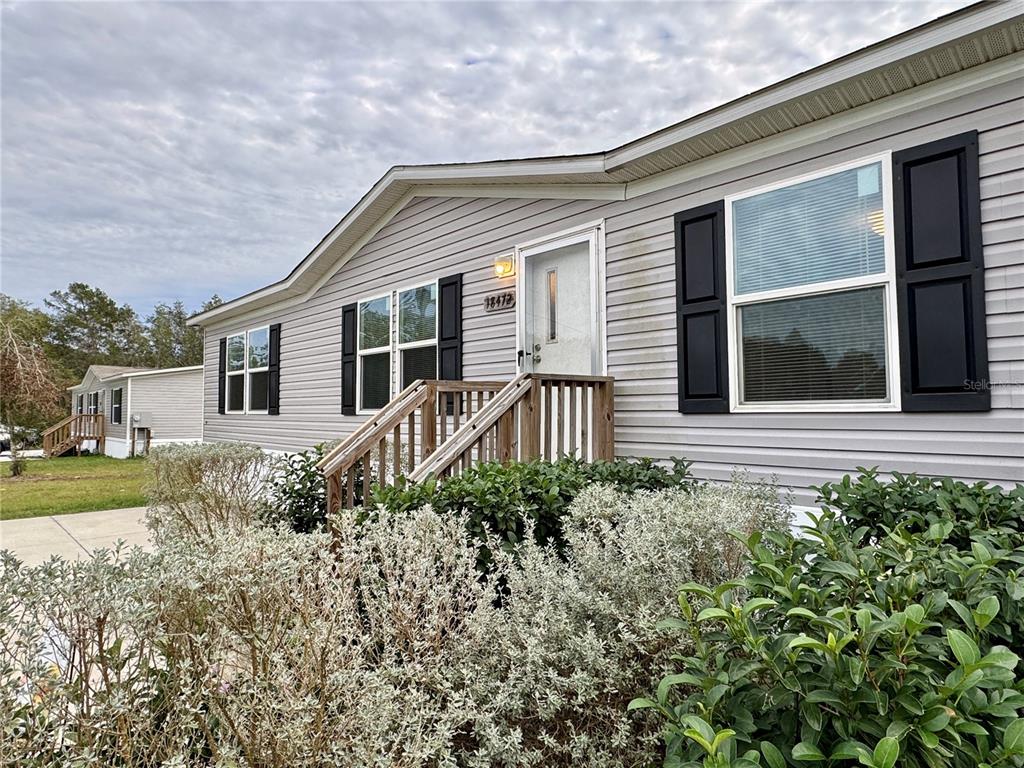A light gray manufactured home features black shutters, a white front door, and wooden stairs — 18472 SE 58TH PLACE, OCKLAWAHA, FL