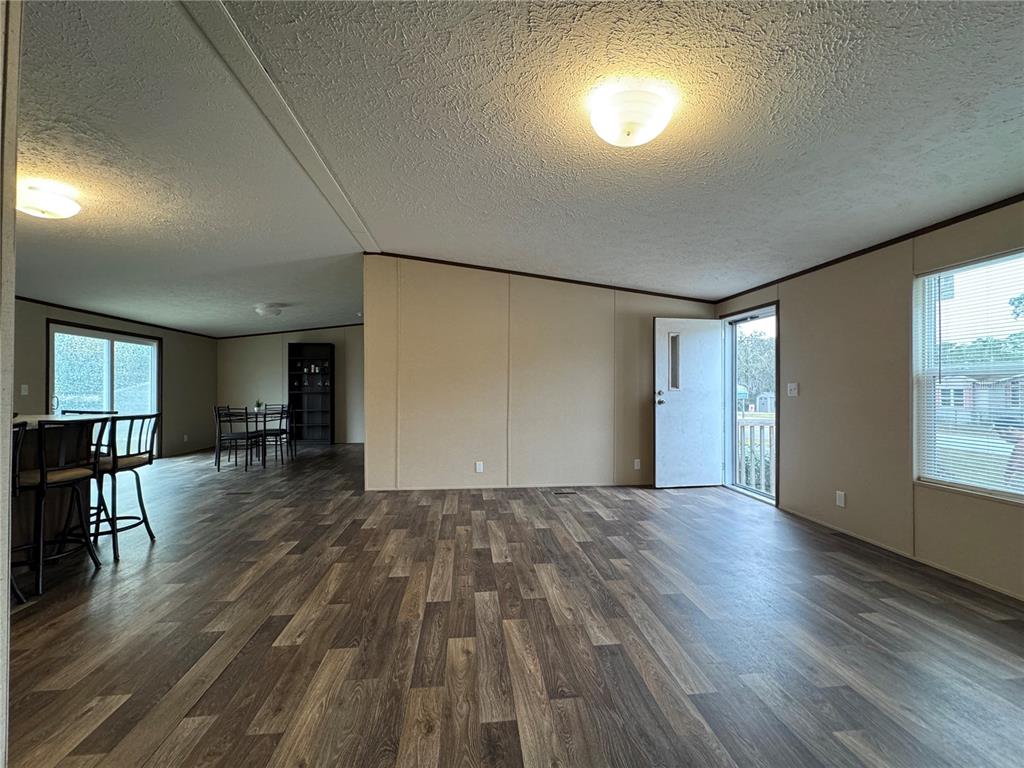 A living room with wood-look flooring, beige walls, and an open doorway to a dining area — 18472 SE 58TH PLACE, OCKLAWAHA, FL