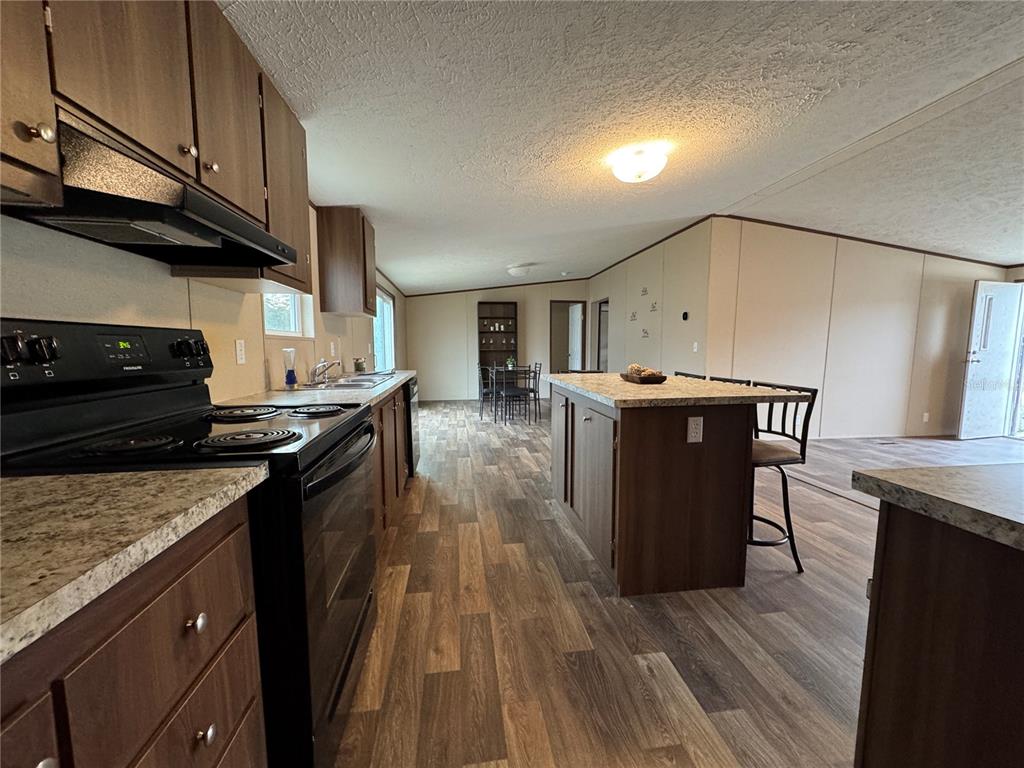 A kitchen features dark wood cabinets, a central island with seating, and wood-look flooring — 18472 SE 58TH PLACE, OCKLAWAHA, FL