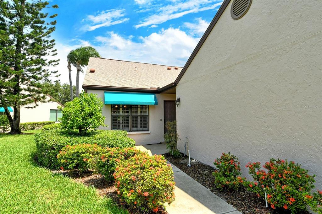 An exterior view of a house entrance with a turquoise awning and landscaped bushes — 6041 CLUBSIDE DRIVE UNIT 6041, SARASOTA, FL