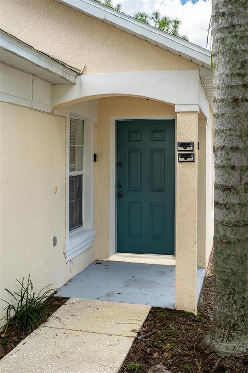 A teal front door is set within a covered entryway of a beige stucco home — 2660 HEMINGWAY AVENUE, HAINES CITY, FL