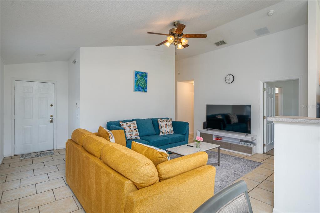 A living room features a yellow sofa, a blue sofa, a television, and tile flooring — 2660 HEMINGWAY AVENUE, HAINES CITY, FL