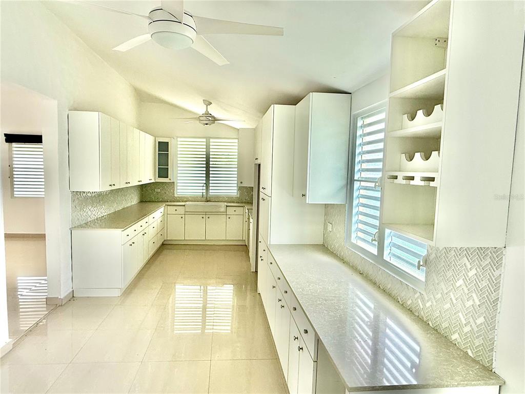 A bright kitchen features white cabinetry, light countertops, a tiled backsplash, and two ceiling fans — 19 C1 UNIT 19, RIO GRANDE, PR