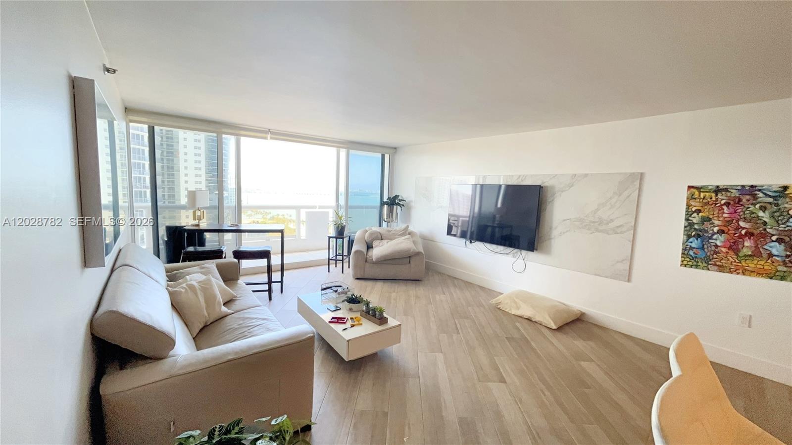 A living room features light wood flooring, a marble-accented television wall, and floor-to-ceiling windows — 1717 N Bayshore Dr # 1951, Miami FL 33132, MIAMI, FL