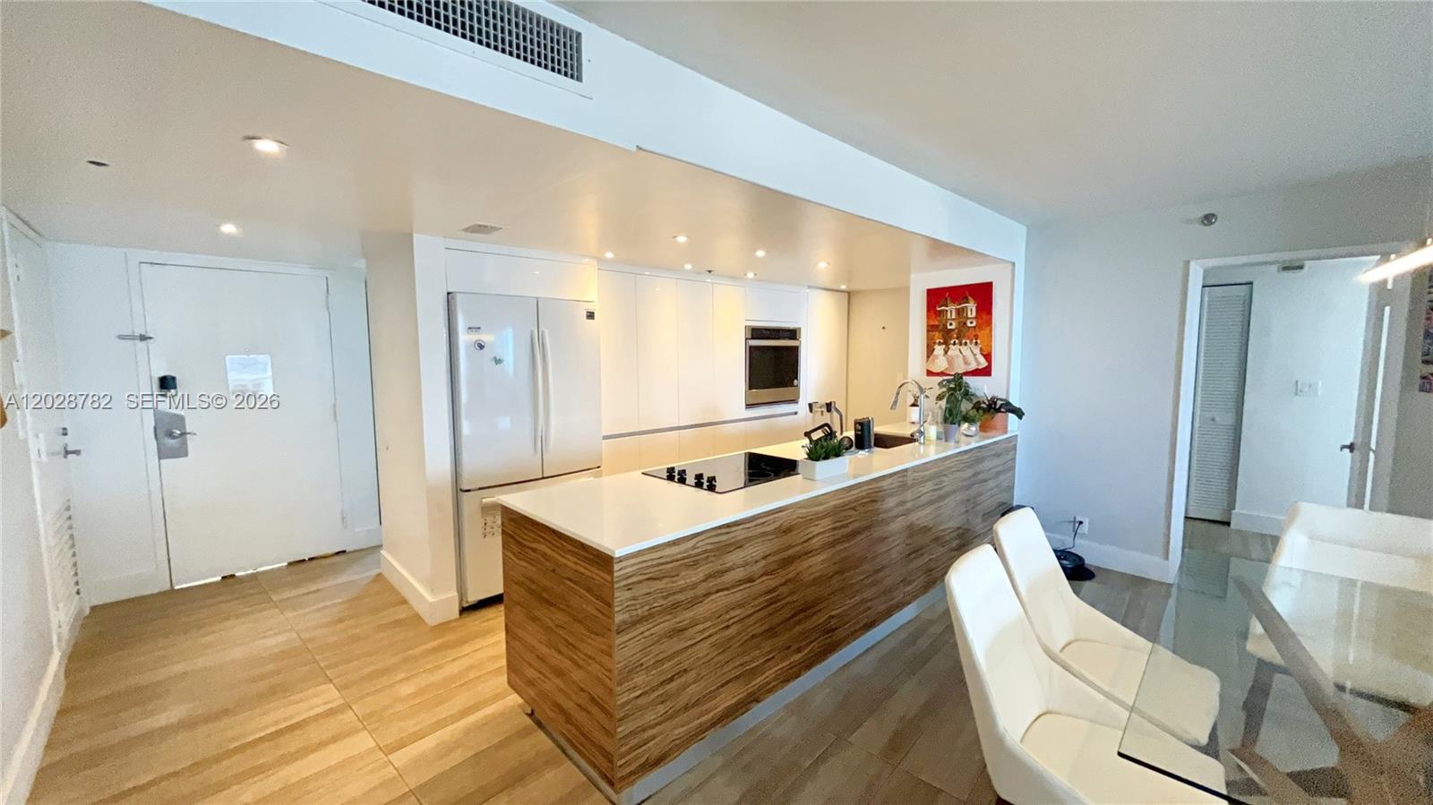 A modern kitchen features white cabinetry, a wood-paneled island, and a glass dining table — 1717 N Bayshore Dr # 1951, Miami FL 33132, MIAMI, FL