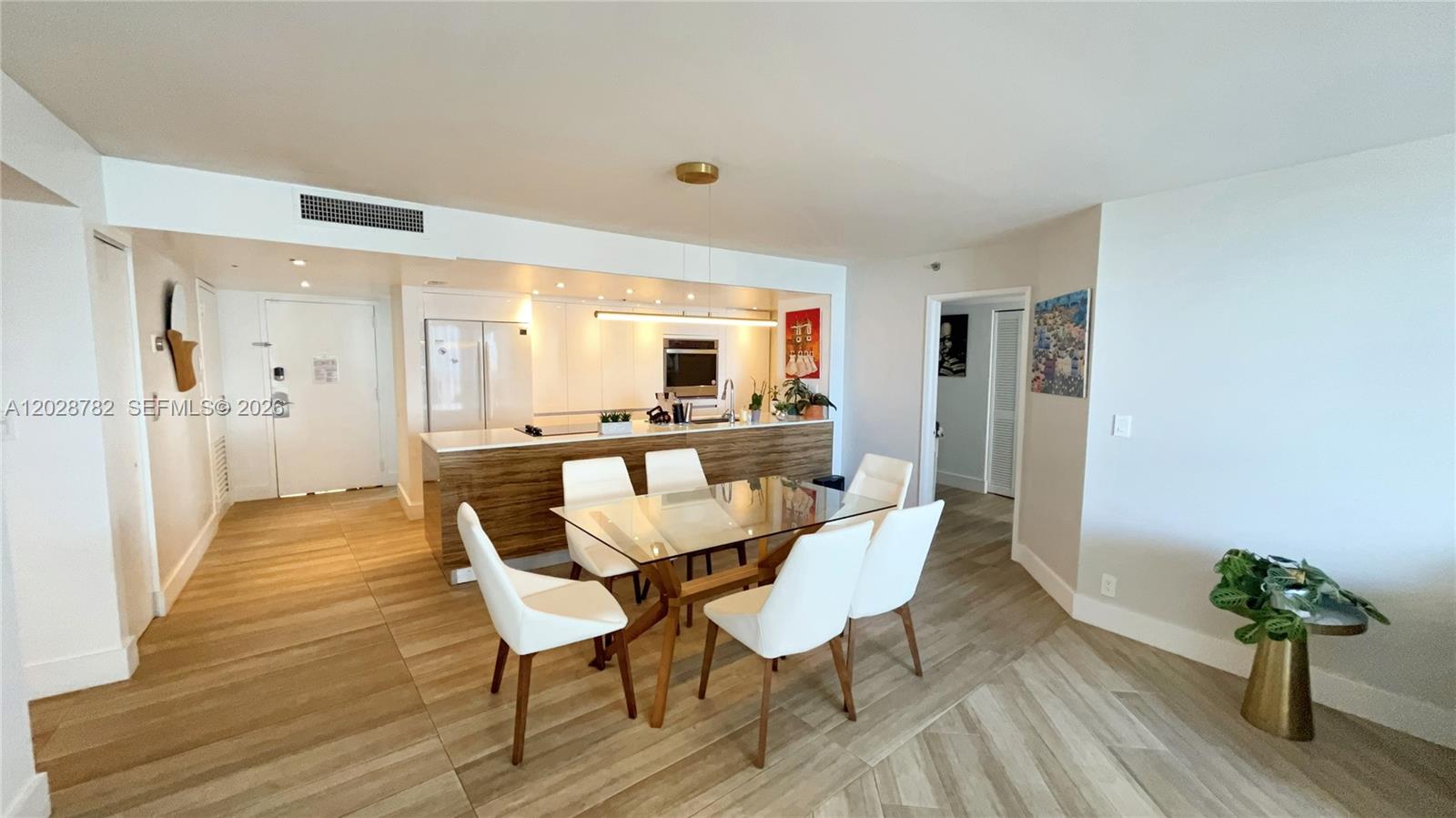 An open-concept kitchen and dining area features a glass table, white chairs, and wood-look flooring — 1717 N Bayshore Dr # 1951, Miami FL 33132, MIAMI, FL