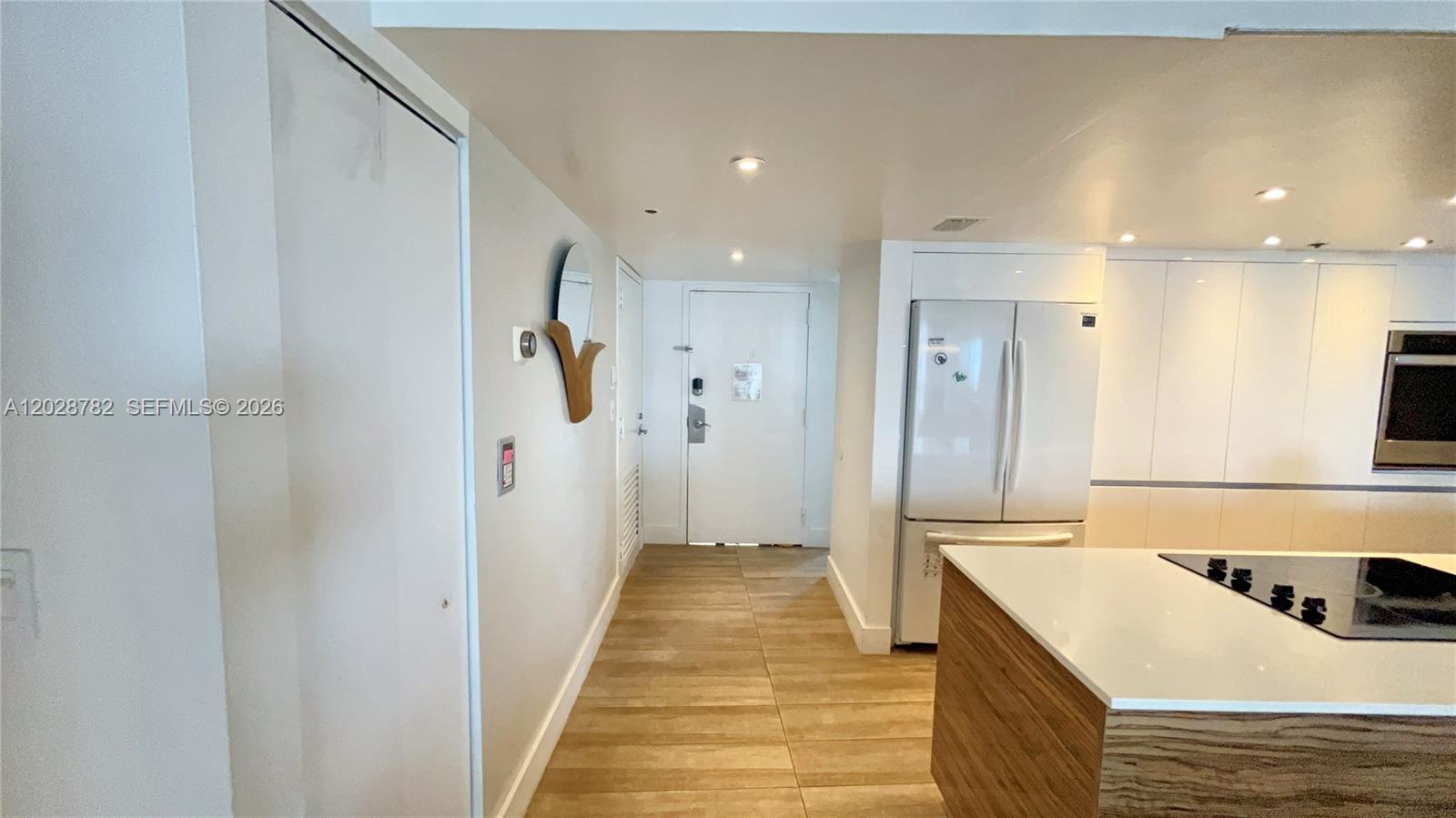 A modern kitchen features white cabinetry, a wood-paneled island, and light-colored tile flooring — 1717 N Bayshore Dr # 1951, Miami FL 33132, MIAMI, FL