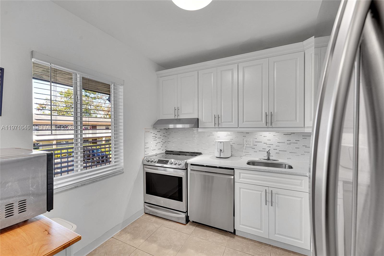 A kitchen features white cabinets, stainless steel appliances, a tiled backsplash, and a large window — 650 NW 80th Ter # 206, Margate FL 33063, MARGATE, FL