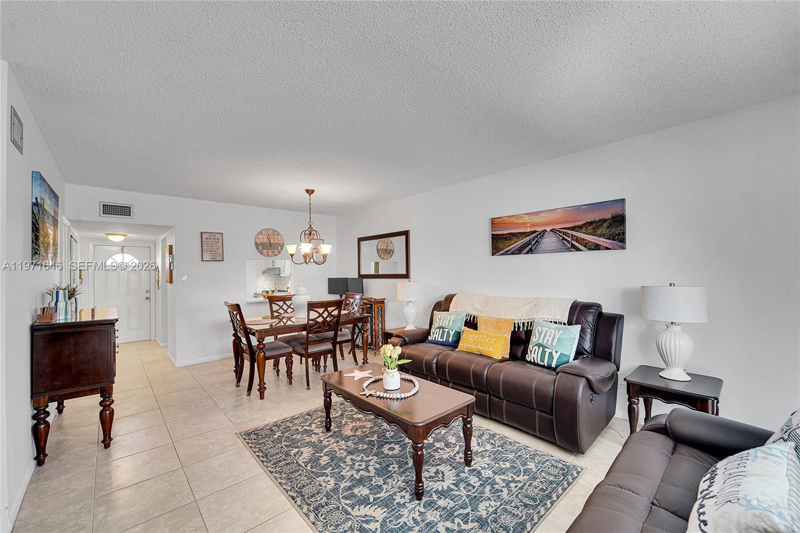 A living and dining area features tile flooring, brown leather furniture, and coastal-themed wall art — 650 NW 80th Ter # 206, Margate FL 33063, MARGATE, FL