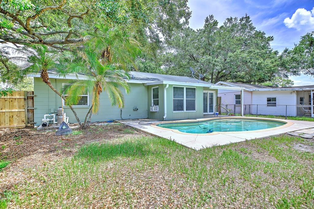 The backyard features a swimming pool, a light green house, and a wooden fence — 1245 HONEYTREE LN E LANE E, LAKELAND, FL