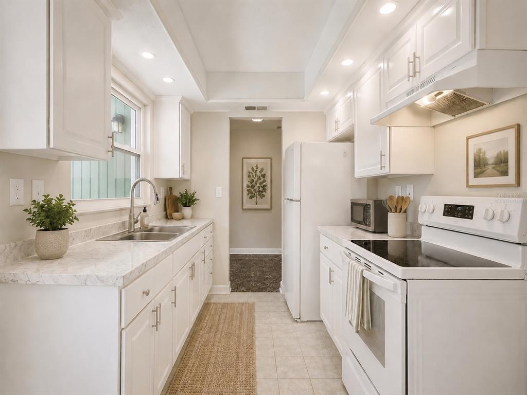 A galley kitchen features white cabinets, marble-look countertops, and white appliances — 1245 HONEYTREE LN E LANE E, LAKELAND, FL