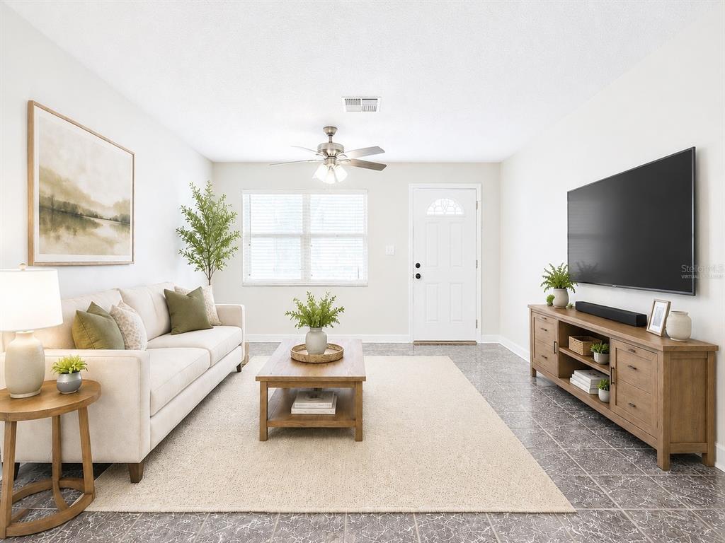 A living room features a beige sofa, wooden coffee table, media console, and tiled floors — 1245 HONEYTREE LN E LANE E, LAKELAND, FL