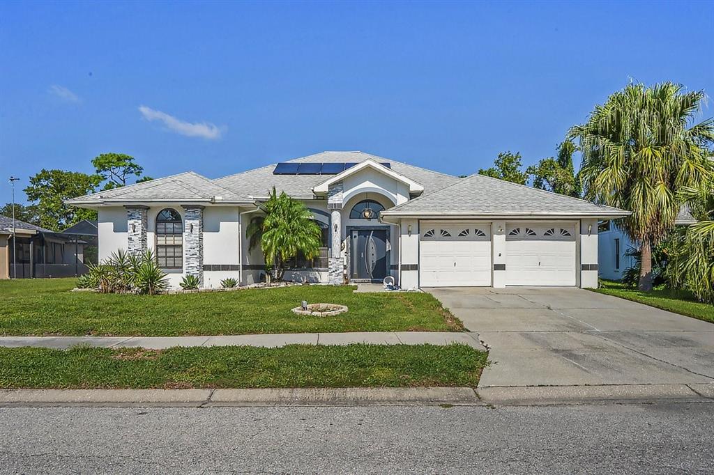A single-story house with a white stucco exterior, a two-car garage, and solar panels — 9301 TOURNAMENT DRIVE, HUDSON, FL