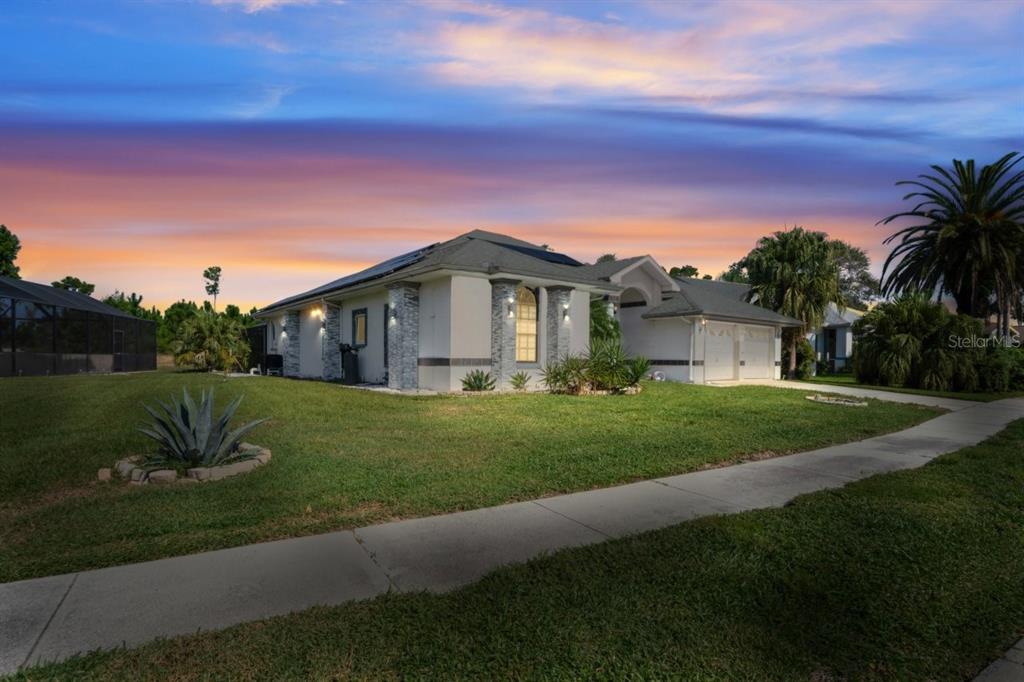A single-story house with a light-colored exterior, stone accents, and a two-car garage at sunset — 9301 TOURNAMENT DRIVE, HUDSON, FL
