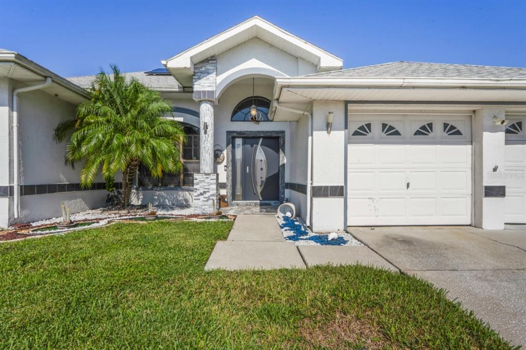 A single-story house with a white stucco exterior, a palm tree, and a gray door — 9301 TOURNAMENT DRIVE, HUDSON, FL