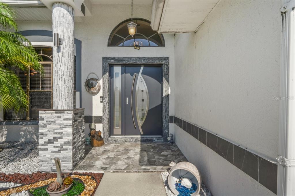 A modern dark gray front door with a glass insert sits under a stone archway — 9301 TOURNAMENT DRIVE, HUDSON, FL