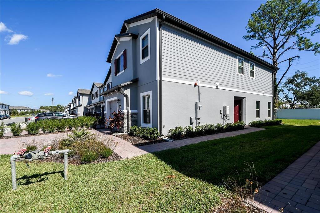 A two-story townhouse with gray siding and a red door sits on a grassy lot — 310 CEDAR BARK LANE, SANFORD, FL