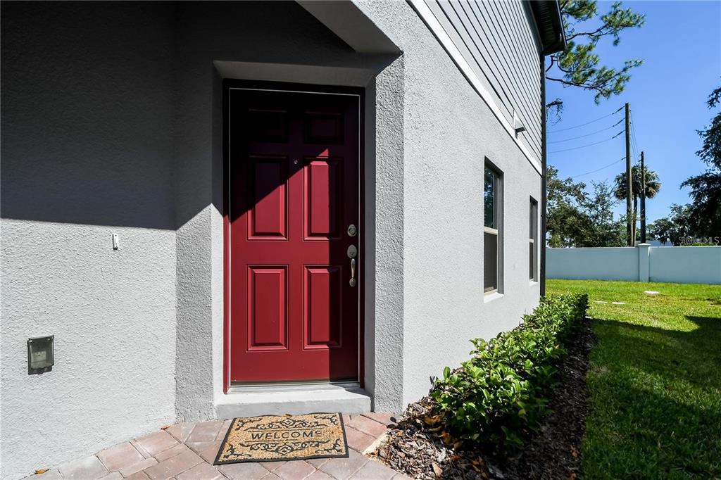 A red front door is set into the light gray stucco exterior of a house — 310 CEDAR BARK LANE, SANFORD, FL