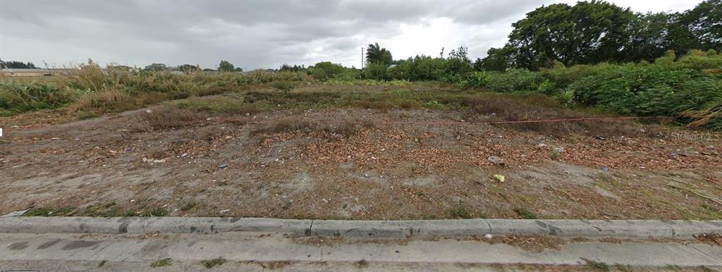 A vacant, overgrown residential lot with a concrete curb in the foreground — 875 JOE LOUIS AVENUE, PAHOKEE, FL