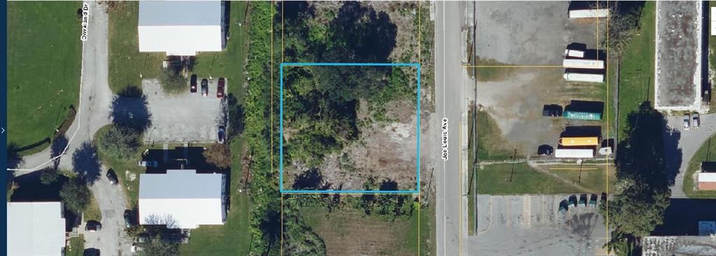 An aerial view shows a vacant, rectangular lot outlined in blue along a paved road — 875 JOE LOUIS AVENUE, PAHOKEE, FL
